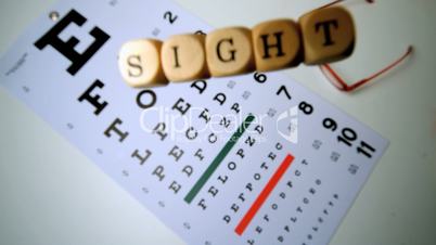 Dice spelling out sight falling onto eye test beside glasses