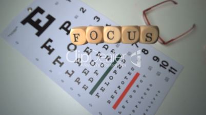 Dice spelling out focus falling onto eye test beside glasses
