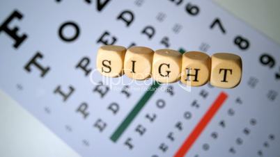 Dice spelling out sight falling onto eye test beside glasses