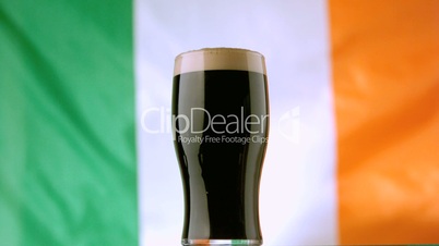 Pint of Irish stout on background of irish flag waving