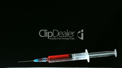 Syringe of blood falling and bouncing on black surface