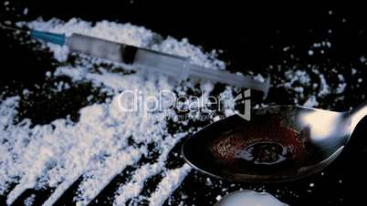 Syringe falling on white drug while drug is cooking on spoon