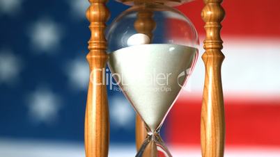 Sand flowing through hourglass with american flag background