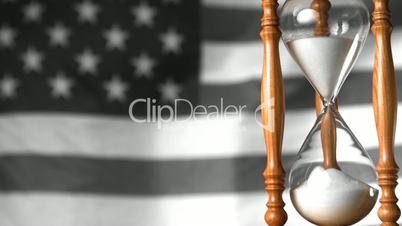 Sand flowing through hourglass with american flag waving in background