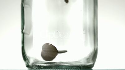 Many coins pouring into glass jar close up on white background