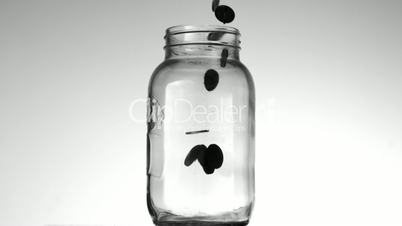 Many coins pouring into glass jar on white background