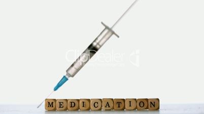 Syringe falling in front of dice spelling medication