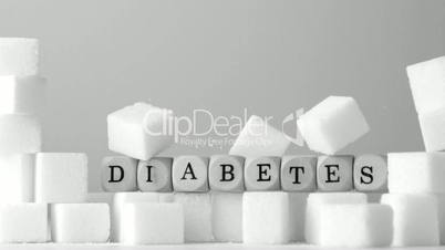 Dice spelling out diabetes falling over sugar cubes in black and white