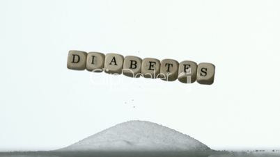 White dice spelling out diabetes falling over pile of sugar on white background