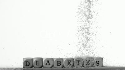 Sugar powder being poured over white dice spelling out diabetes