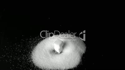 Two sugar cubes falling into pile of sugar on black surface