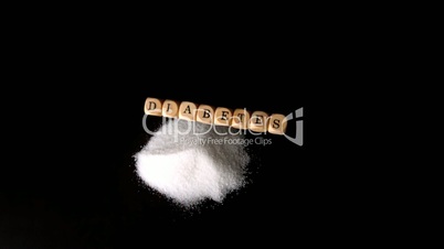 Dice spelling out diabetes falling over a pile of sugar on black surface