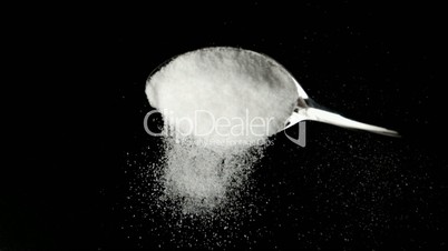 Spoon pouring sugar powder on black surface