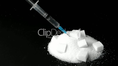 Syringe of insulin falling into pile of sugar with sugar cubes in it