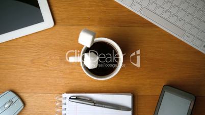 Sugar cubes falling into cup of coffee and splashing a tablet pc