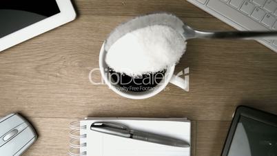 Sugar in teaspoon falling into cup of coffee on a desk