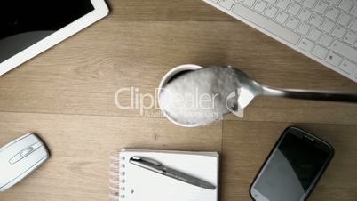 Teaspoon of sugar powder being spilled into and around a cup of coffee