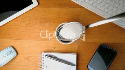 Teaspoon with sugar falling into a cup of coffee and splashing a desk with tablet pc