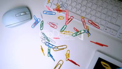 Colourful paperclips falling in the middle of a white office desk