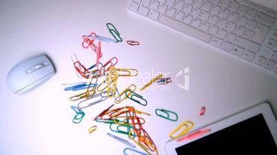 Colourful paperclips falling on office desk