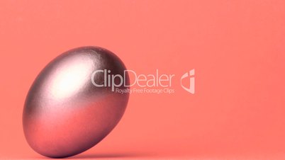 Shiny egg rolling across pink surface