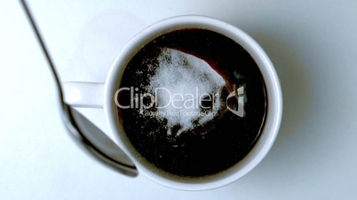 Teaspoon pouring sugar into cup of coffee