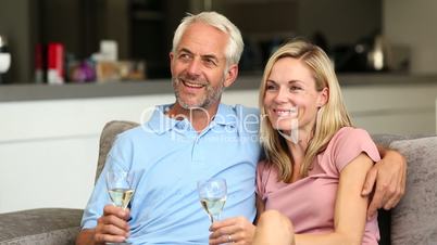 Couple watching tv while holding white wine glass