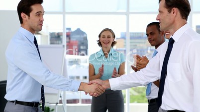 Businessmen shake hands while other business people applauding