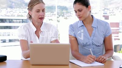Two businesswomen working together while using a laptop