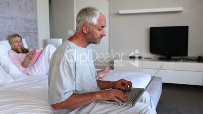 Couple relaxing in bed and man doing his own thing