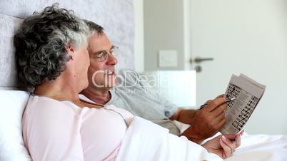Mature couple solving crossword in the bed