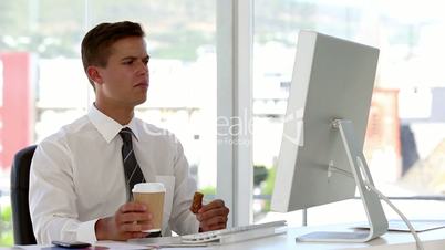 Young businessman eating and drinking while he works on his computer