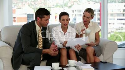 Three business people on a sofa looking at a document