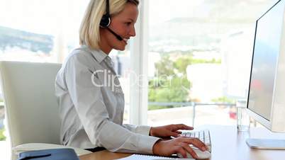 Businesswoman speaking on headset and typing