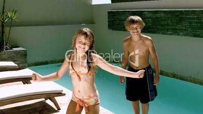 Young girl dancing while brother jumping in the swimming pool