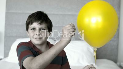 Boy piercing his balloon in the bedroom in selective color