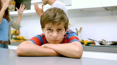Sad boy with arms folded while parents quarreling