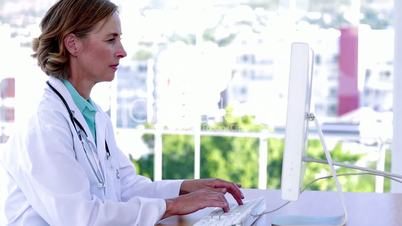 Doctor typing at her desk and smiling