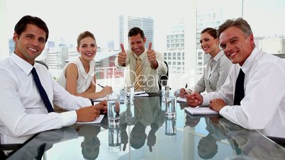 Laughing businessman giving thumbs up with colleagues around