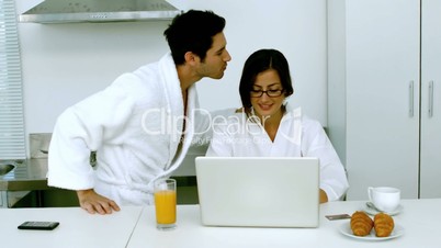 Man kissing his girlfriend while she is taking her breakfast