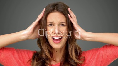 Frustrated woman holding her head between hands on grey background