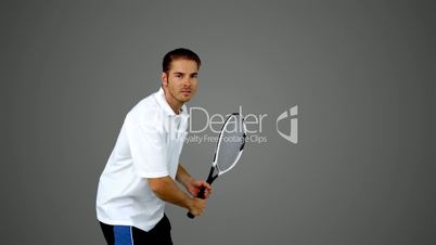 Attractive man playing tennis on grey screen