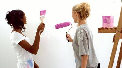 Two women painting on white wall