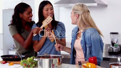 Laughing friends singing into a wooden spoon while cooking