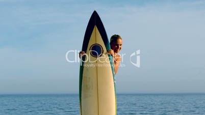 Female surfer peeking from behind her board