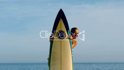 Female surfer peeking out from behind her board