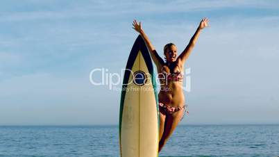 Female surfer jumping out from behind her board