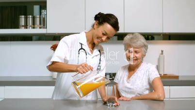 Home nurse pouring orange juice for patient in kitchen