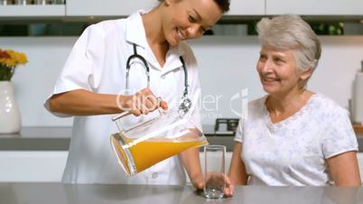 Home help pouring orange juice for patient in kitchen