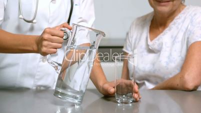 Home help pouring water for patient in kitchen